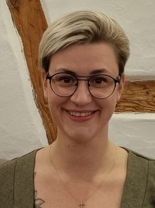 Lächelndes Porträt einer Person mit kurzer blonder Frisur und runder Brille